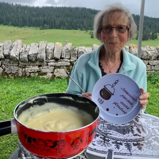 dame senior devant une fondue tenant une assiette et souriante